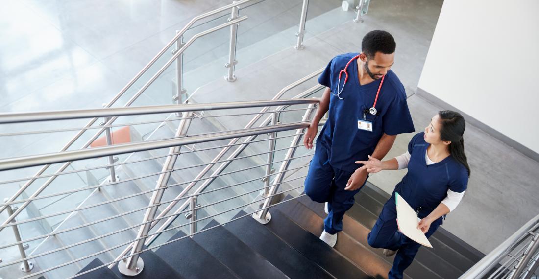 Two health care workers speak to each other while walking up the stairs.