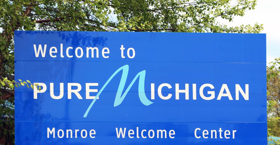Blue sign that reads "Welcome to Pure Michigan" with the text "Monroe Welcome Center" at the bottom of the sign.