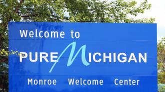 Blue sign that reads "Welcome to Pure Michigan" with the text "Monroe Welcome Center" at the bottom of the sign.